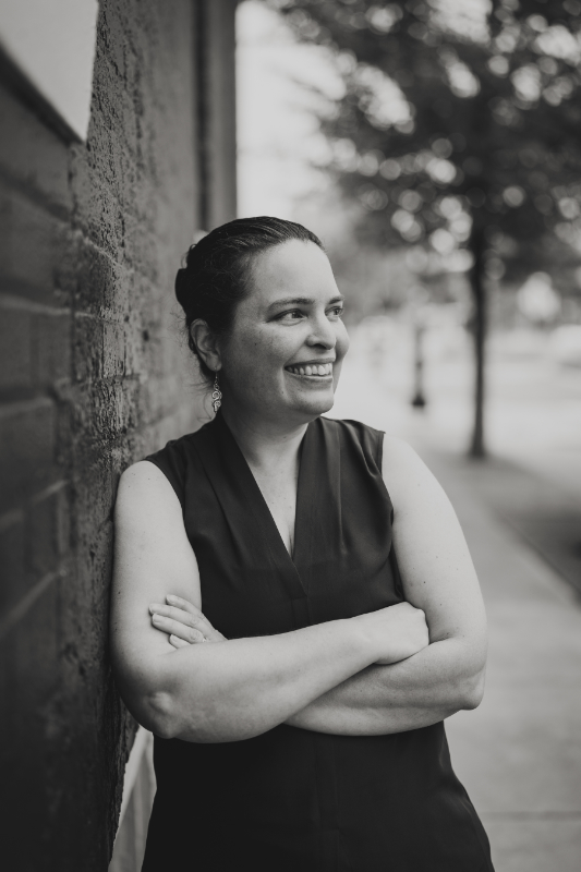 A black-and-white photo of me looking away from a painted brick wall. My earrings are snakes.