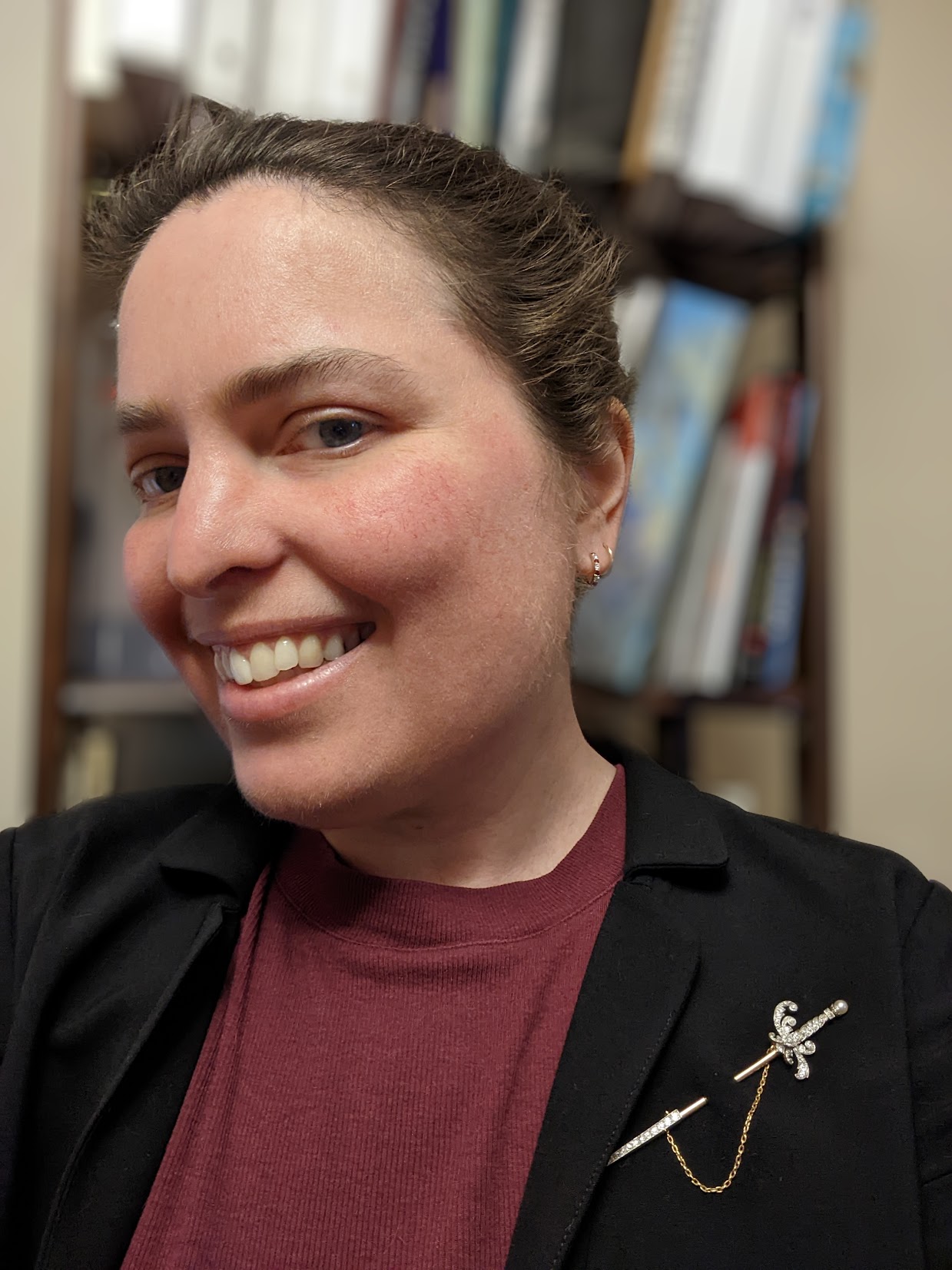 A close-up where I'm wearing a diamond pin shaped like a rapier and standing in front of a bookcase